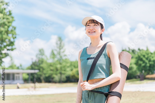 公園でヨガマットを持った帽子とスポーツウェアのアジア人女性 