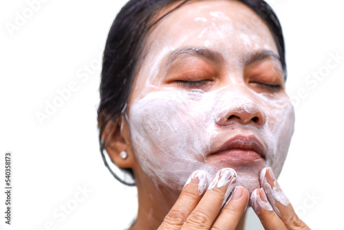 Asian woman with olive or tanned skin does facial treatment by applying spa mask cream on her face