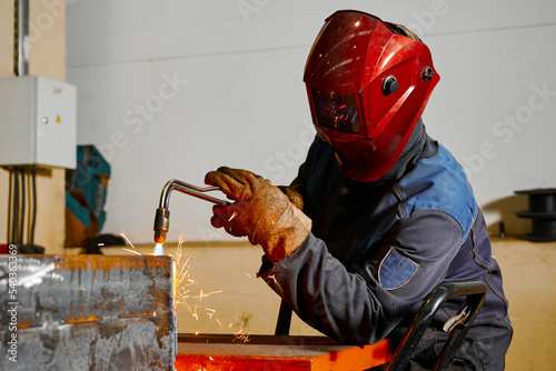 Welder in mask cuts steel beam with cutting blowpipe in shop photo