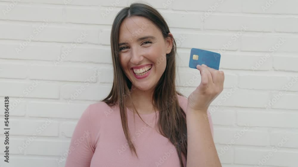 Young beautiful hispanic woman smiling confident holding credit card over isolated white brick background Young beautiful hispanic woman smiling confident holding credit card over isolated white brick background