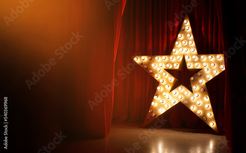 Photo of golden star with light bulbs on red velvet curtain on stage © Glebstock