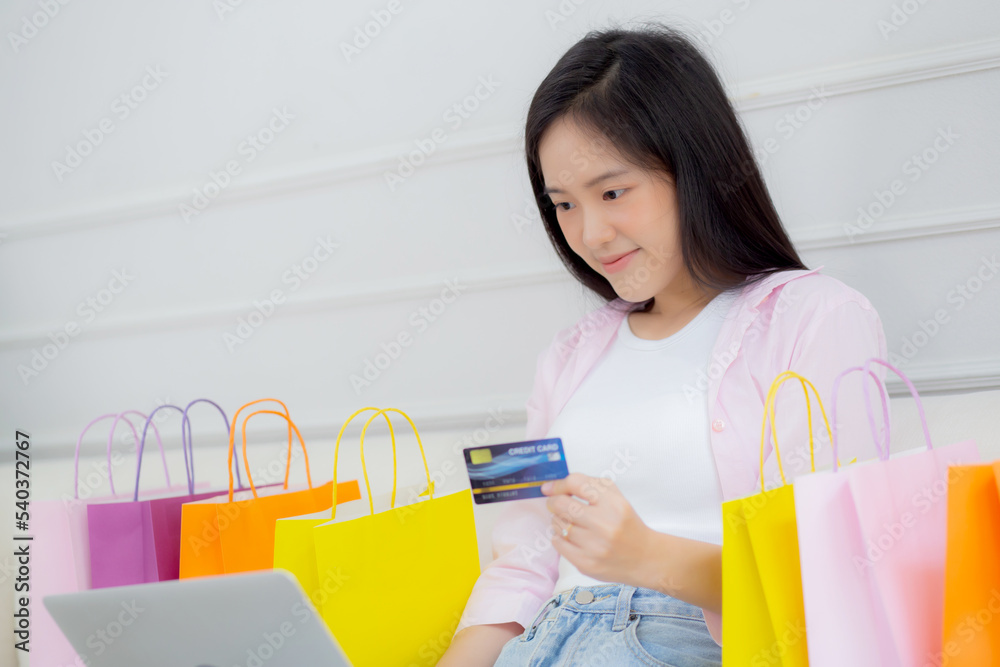 Young asian woman sitting on sofa using laptop computer shopping online with credit card buying to internet, happiness girl paying with transaction financial, purchase and payment, business concept. Young asian woman sitting on sofa using laptop computer shopping online with credit card buying to internet, happiness girl paying with transaction financial, purchase and payment, business concept.