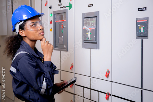 Electrical young asian woman engineer examining maintenance cabinet system electric and using tablet in control room at industrial factory, technician or electrician inspection power distribution.