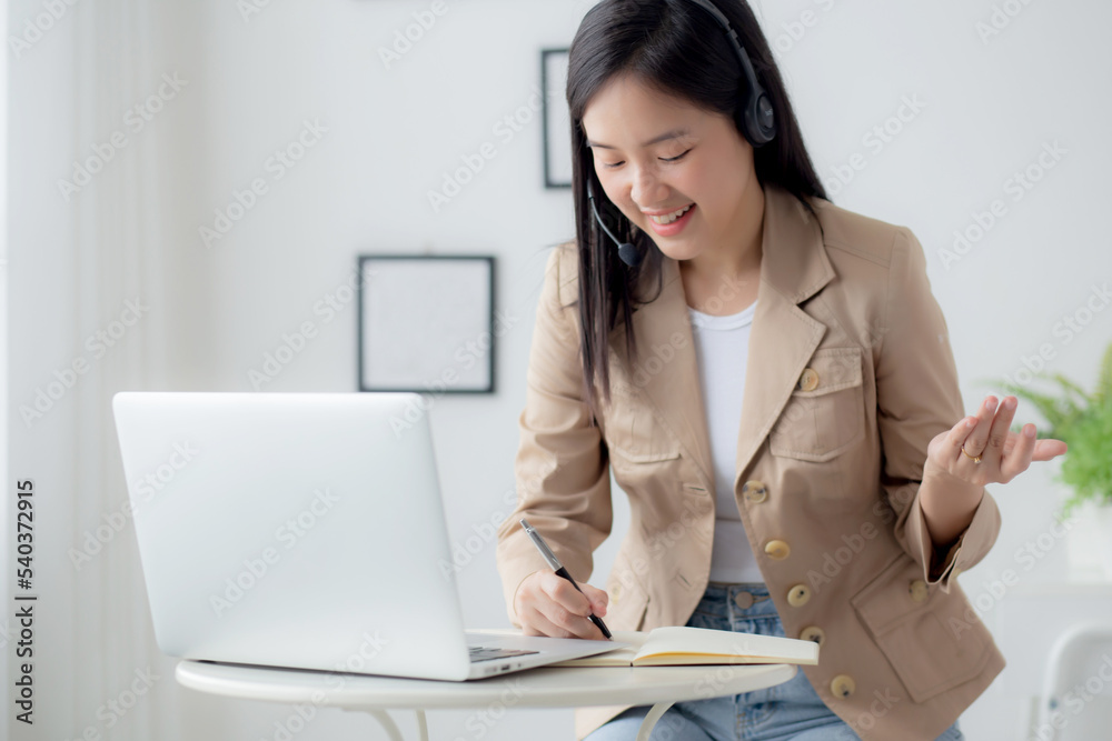Young asian woman using laptop computer for working from home and video call conference online and writing on note at home, female meeting distant and service representative, business concept. Young asian woman using laptop computer for working from home and video call conference online and writing on note at home, female meeting distant and service representative, business concept.
