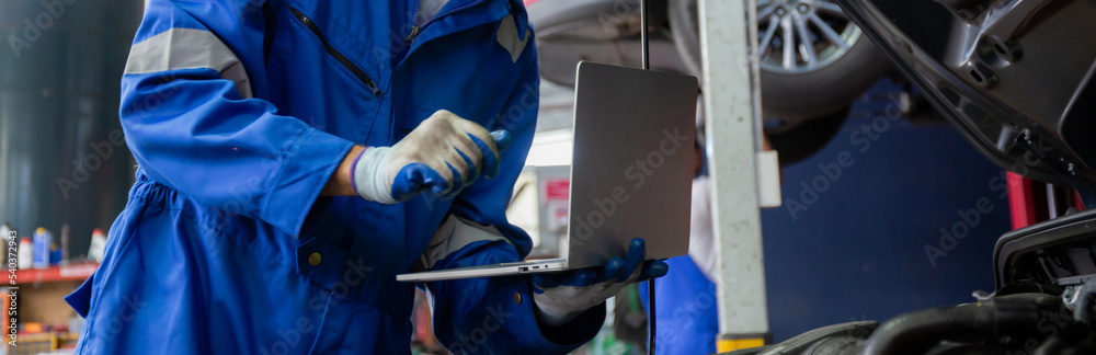 Young man is mechanic using laptop computer checking engine of car in the garage, worker examining and diagnostic automobile, technician and maintenance of vehicle, transport concept. Young man is mechanic using laptop computer checking engine of car in the garage, worker examining and diagnostic automobile, technician and maintenance of vehicle, transport concept.