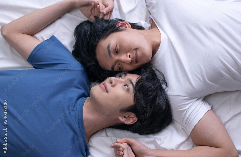 High angle view of smiling Asian gay couple relaxing and lying down in bed. LGBT male couple lifestyle concept. High angle view of smiling Asian gay couple relaxing and lying down in bed. LGBT male couple lifestyle concept.