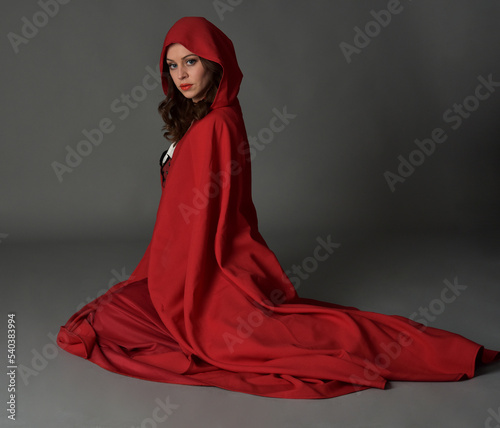 фотографія Full length portrait of beautiful brunette woman wearing red medieval fantasy costume with long skirt &  flowing hooded cloak