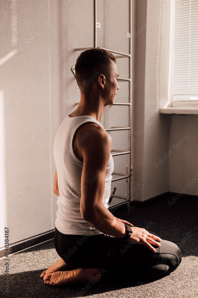 A man in a T-shirt performs morning exercises sitting in front of the window A man in a T-shirt performs morning exercises sitting in front of the window