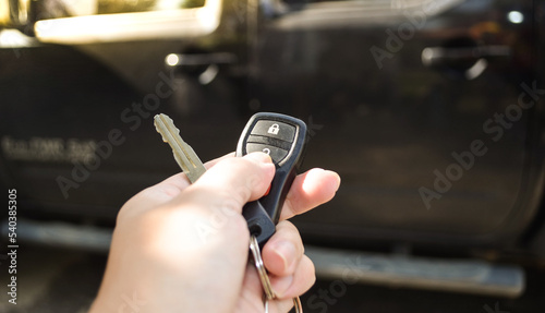 Close up hand of man holding and push car remote control for lock and Un-lock old black car ,Car key and  remote.
