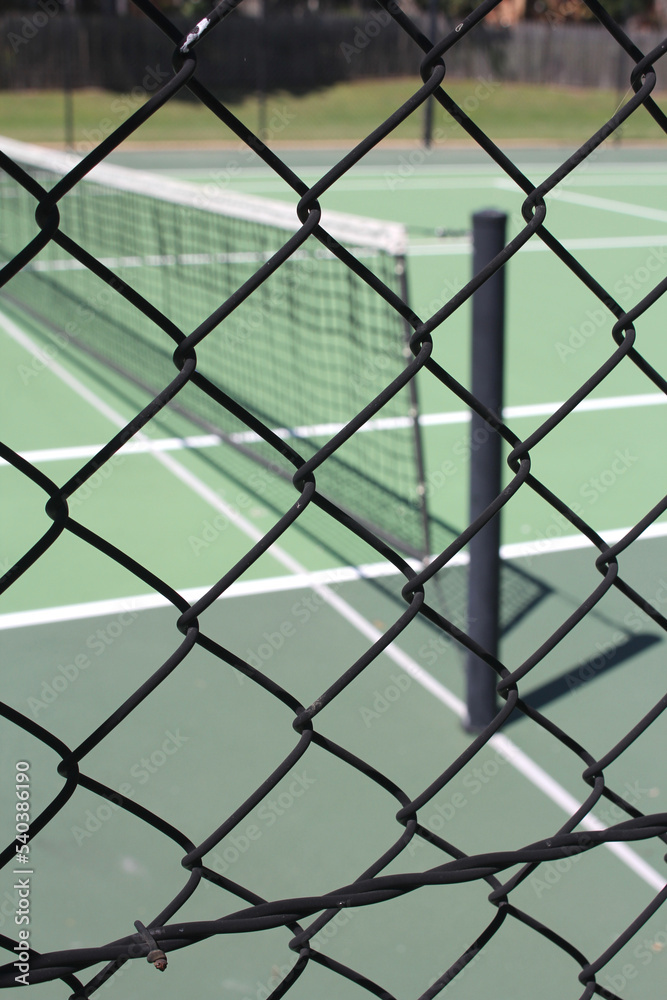Abstract view of all weather green tennis court, looking through diamond wire fencing Abstract view of all weather green tennis court, looking through diamond wire fencing