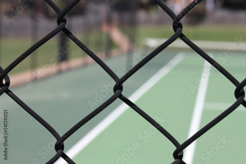 Abstract view of all weather green tennis court, looking through diamond wire fencing