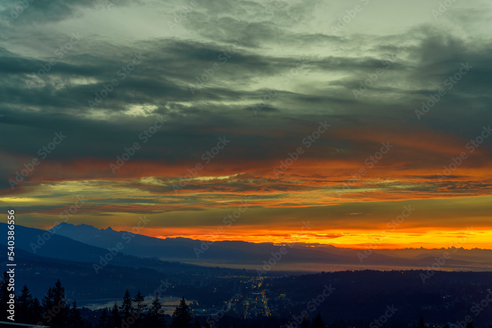 Sunrise over Fraser Valley and Burrard Inlet, BC, in the pre-dawn, with alpine mountains in silhouette on horizon.
