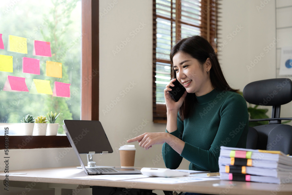 Smiling beautiful Asian businesswoman analyzing chart and graph showing changes on the market and holding smartphone at office. Smiling beautiful Asian businesswoman analyzing chart and graph showing changes on the market and holding smartphone at office.