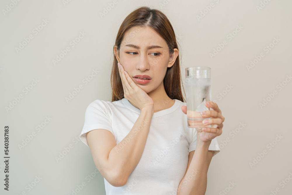 Suffering from toothache, asian young woman, girl touch cheek, face expression ache or feel pain, sensitive molar teeth, hand holding glass of water with ice, inflammation when drink cold, healthcare.