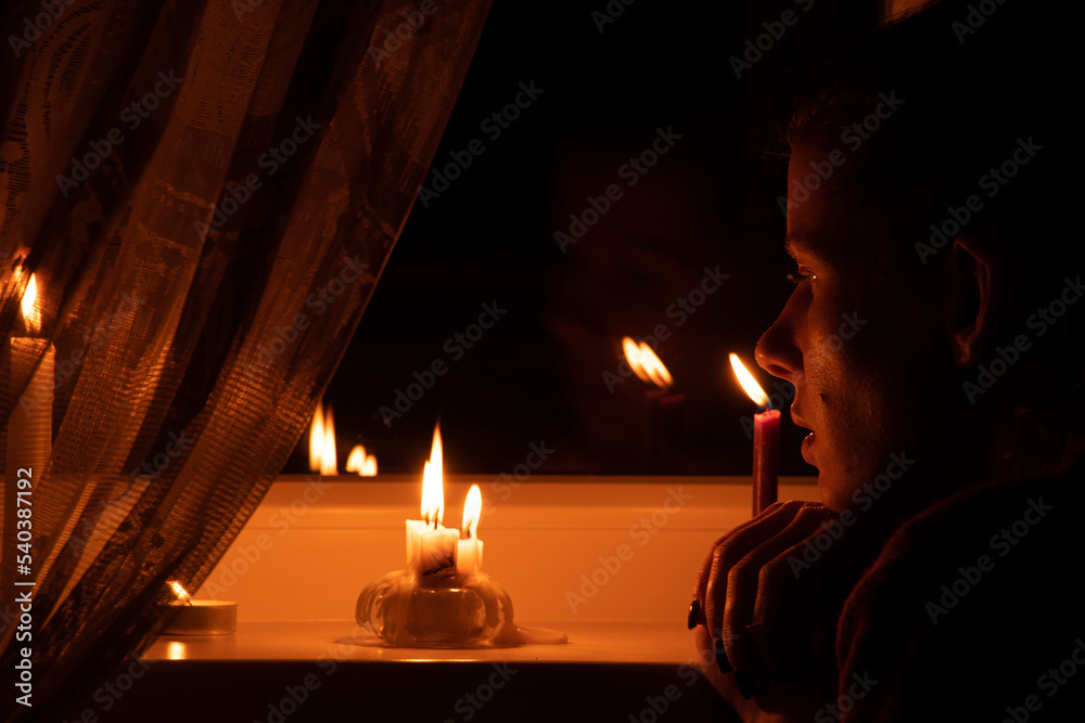 The girl's face put candles on the window in an apartment in Ukraine, Ukraine without electricity because of the war, an apartment without light 2022 The girl's face put candles on the window in an apartment in Ukraine, Ukraine without electricity because of the war, an apartment without light 2022