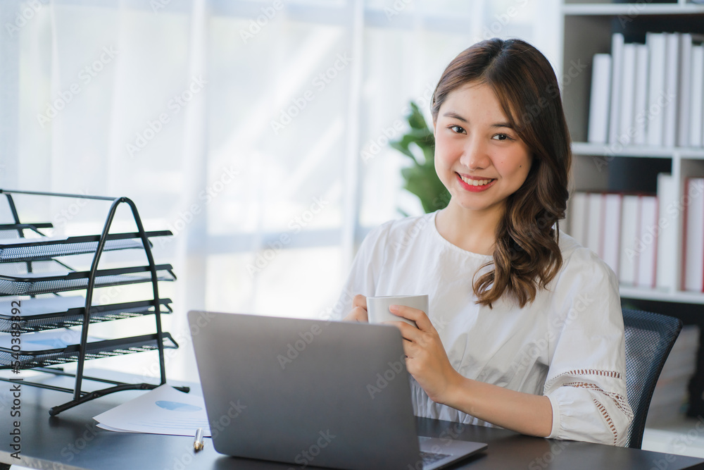Beautiful Asian businesswoman working on a desk with a laptop with a smiling face while looking at the document received in the office. Beautiful Asian businesswoman working on a desk with a laptop with a smiling face while looking at the document received in the office.