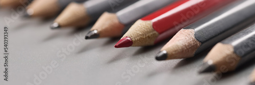 Pencils tips put on grey surface in strict order, red one among black pens photo