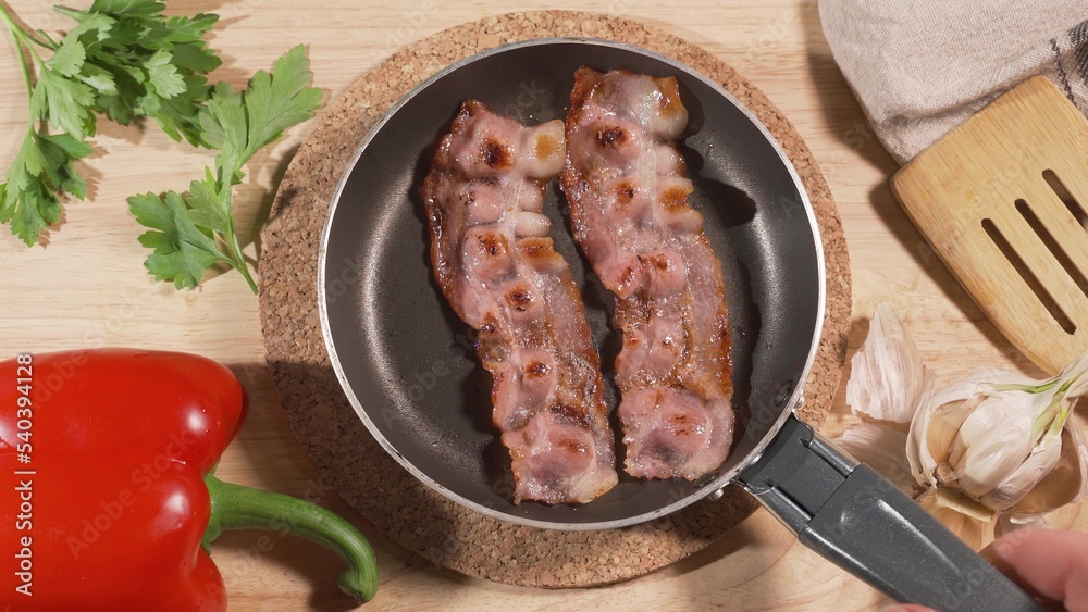 The cook puts on a served table a frying pan with fried eggs and bacon. On the table are greens and red pepper. European breakfast or lunch concept The cook puts on a served table a frying pan with fried eggs and bacon. On the table are greens and red pepper. European breakfast or lunch concept