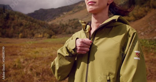 Active woman hiker standing outdoors in nature, zipping up a jacket. Close-up footage