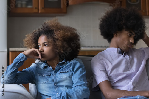 Sad silent African teenagers sit on sofa at home separately after quarrel. Young pensive couple thinks over troubles in relations, having difficulties in relationships. First love, quarrels, jealousy