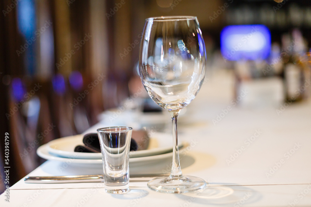 Close up new white porcelain tableware plates on purple place mats and empty wine glasses ready for dinner. Table settings wait for guests at home or restaurant.