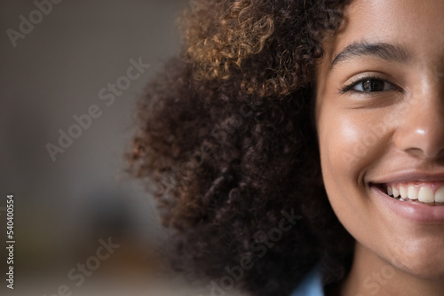 Closeup cropped front half face view of beautiful African teenage girl having natural afro curly hairs and charming wide toothy smile looks at camera. Advertises dental clinic services, gen Z person
