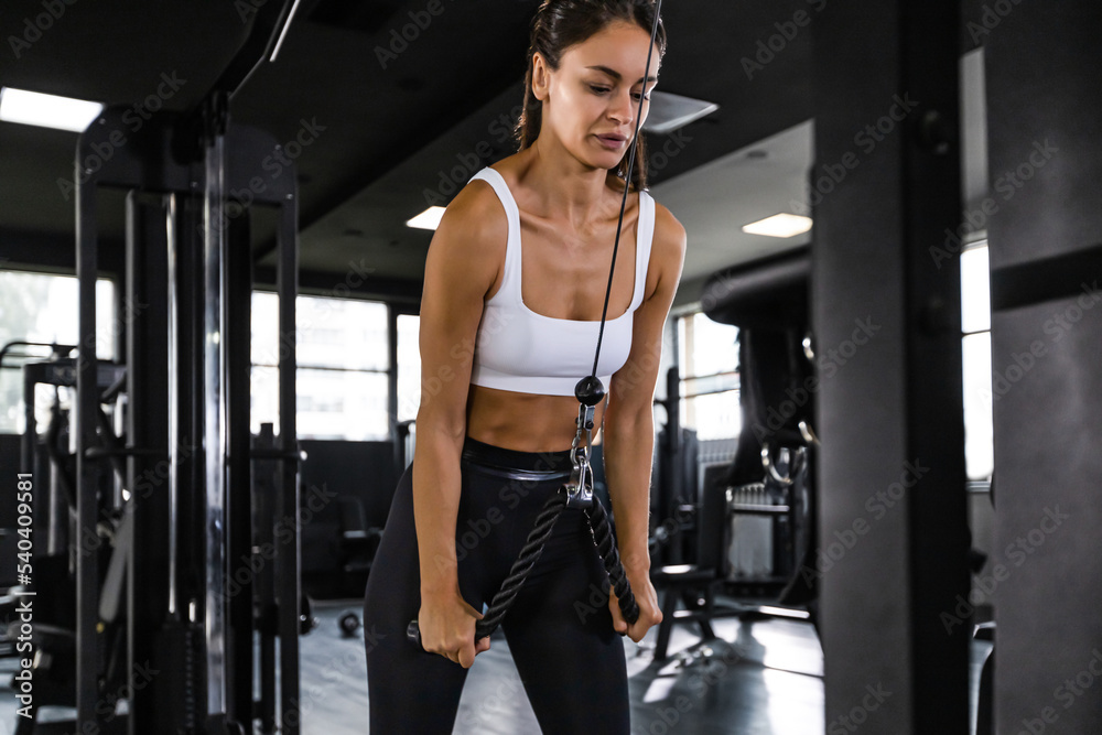 Athletic woman in sportswear doing exercise on the triceps on the crossover machine in the gym. Athletic woman in sportswear doing exercise on the triceps on the crossover machine in the gym.