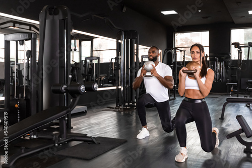 Attractive sports people, african man and caucasian woman, are working out with dumbbells at gym.