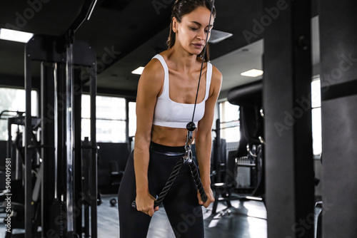 Athletic woman in sportswear doing exercise on the triceps on the crossover machine in the gym.