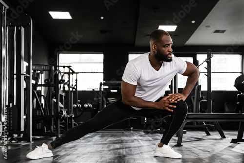 Muscular african man at the gym doing stretching exercises on the floor.