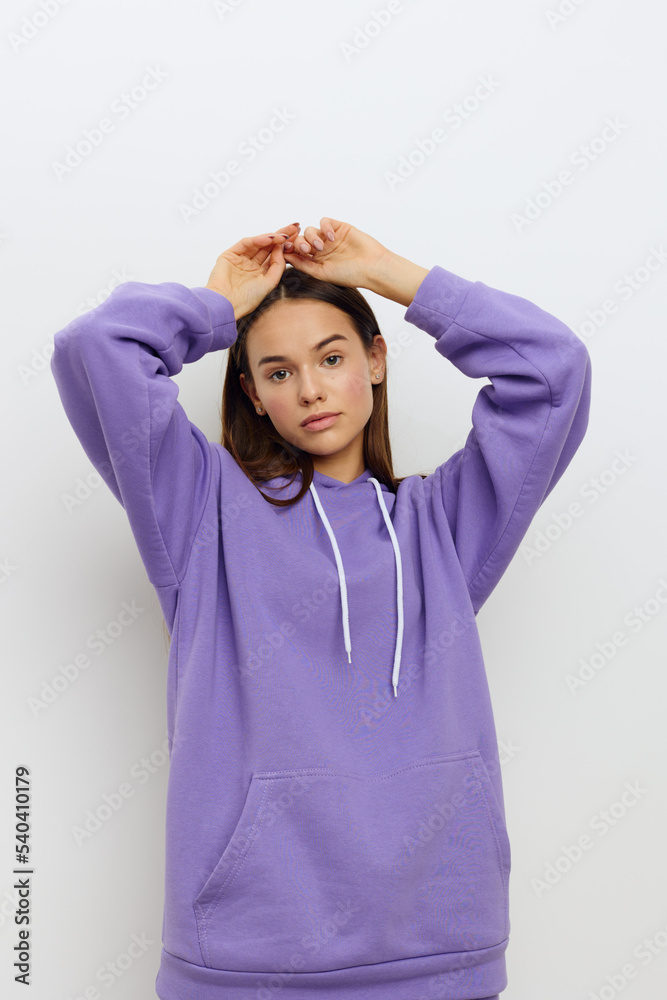 a relaxed woman stands on a white background in a purple suit calmly looks forward with her mouth slightly open hides her hands behind her head