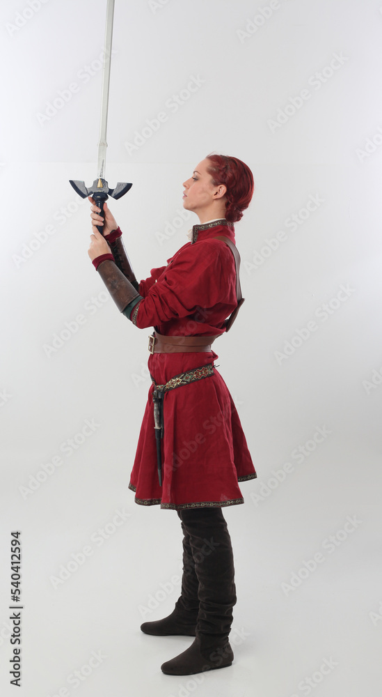 full length portrait of beautiful woman wearing a red medieval fantasy warrior costume with leather armour, holding weapons. Standing pose isolated on white studio background. full length portrait of beautiful woman wearing a red medieval fantasy warrior costume with leather armour, holding weapons. Standing pose isolated on white studio background.