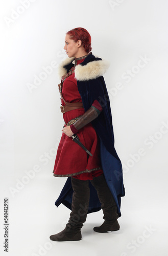 full length portrait of beautiful woman wearing a red medieval fantasy warrior costume with leather armour, holding weapons. Standing pose isolated on white studio background.