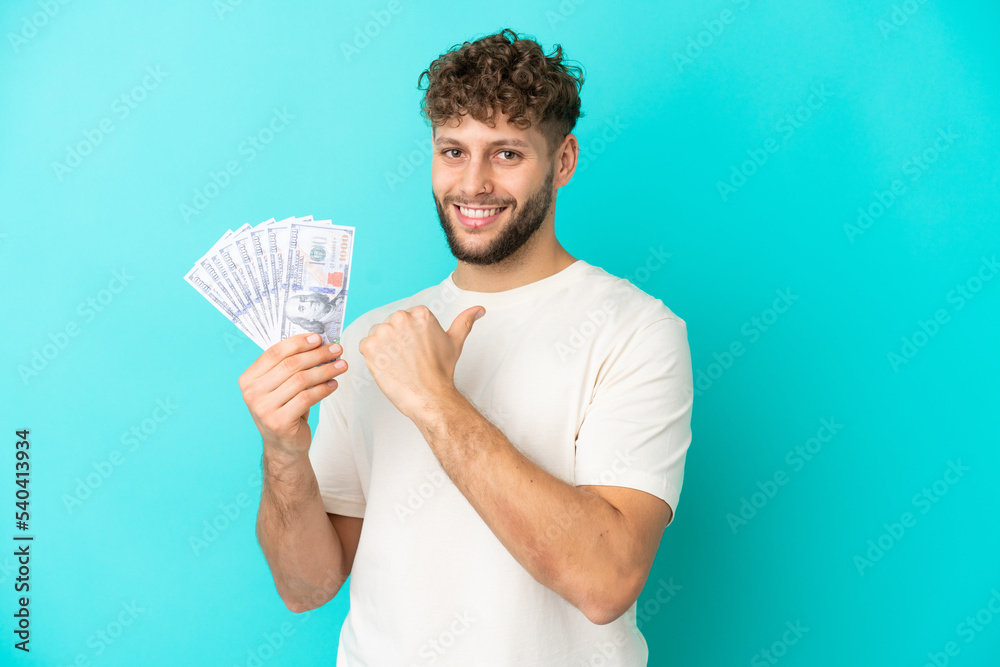 Young caucasian man taking a lot of money isolated on blue background proud and self-satisfied Young caucasian man taking a lot of money isolated on blue background proud and self-satisfied