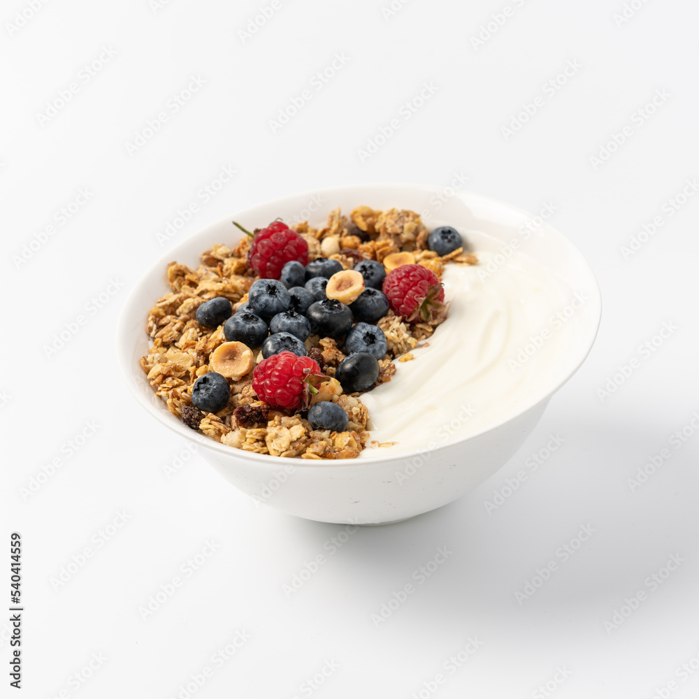 Granola with oatmeal, hazelnuts, raspberries, blueberries and yogurt in white bowl on light background. Morning healthy fast homemade breakfast concept. Isolate with copy space Granola with oatmeal, hazelnuts, raspberries, blueberries and yogurt in white bowl on light background. Morning healthy fast homemade breakfast concept. Isolate with copy space