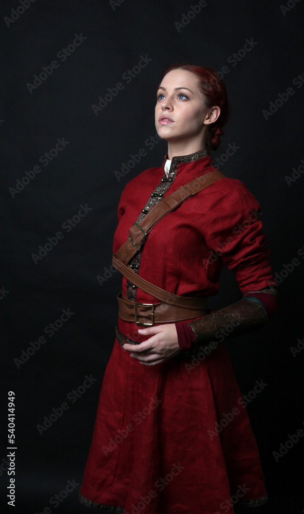 portrait of beautiful woman wearing a red medieval fantasy warrior costume with leather armour. Standing pose isolated on studio background. portrait of beautiful woman wearing a red medieval fantasy warrior costume with leather armour. Standing pose isolated on studio background.