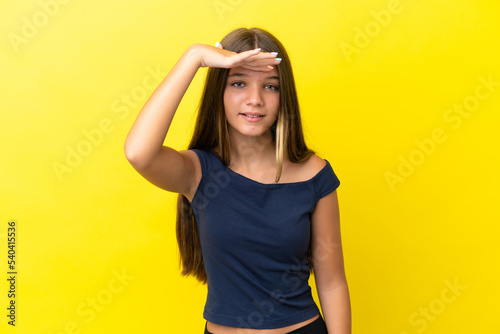 Little caucasian girl isolated on yellow background looking far away with hand to look something