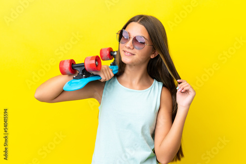 Little caucasian skater girl isolated on yellow background with a skate