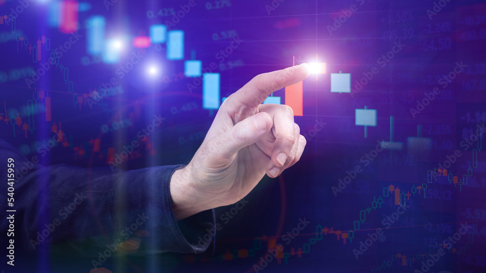 The trader points his finger at the stock chart on the monitor The trader points his finger at the stock chart on the monitor