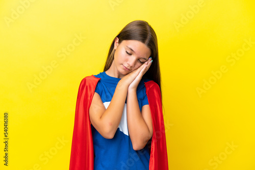 Little caucasian superhero girl isolated on yellow background making sleep gesture in dorable expression