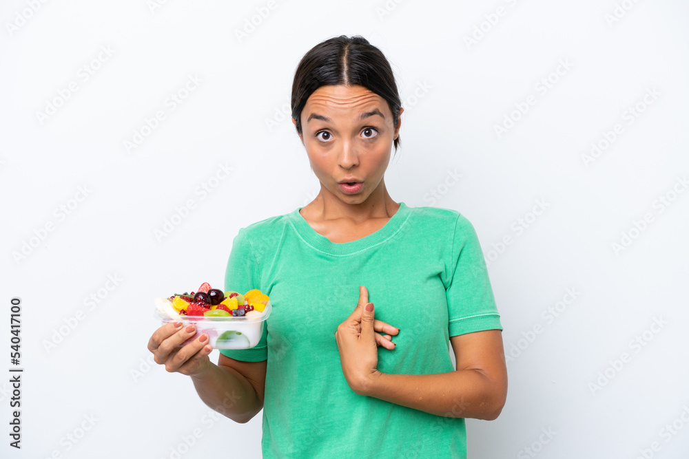 Young hispanic woman holding a bowl of fruit isolated on white background with surprise facial expression Young hispanic woman holding a bowl of fruit isolated on white background with surprise facial expression