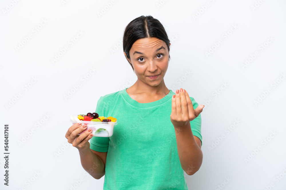 Young hispanic woman holding a bowl of fruit isolated on white background inviting to come with hand. Happy that you came Young hispanic woman holding a bowl of fruit isolated on white background inviting to come with hand. Happy that you came