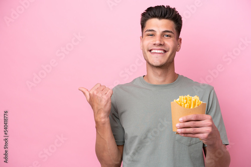 Young caucasian man holding fried chips isolated on pink background pointing to the side to present a product © luismolinero