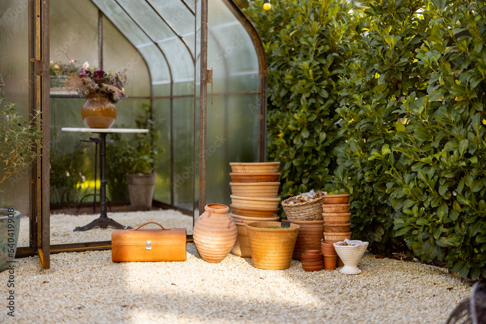 Empty clay pots ready for planting in garden with greenhouse on background outdoors Empty clay pots ready for planting in garden with greenhouse on background outdoors
