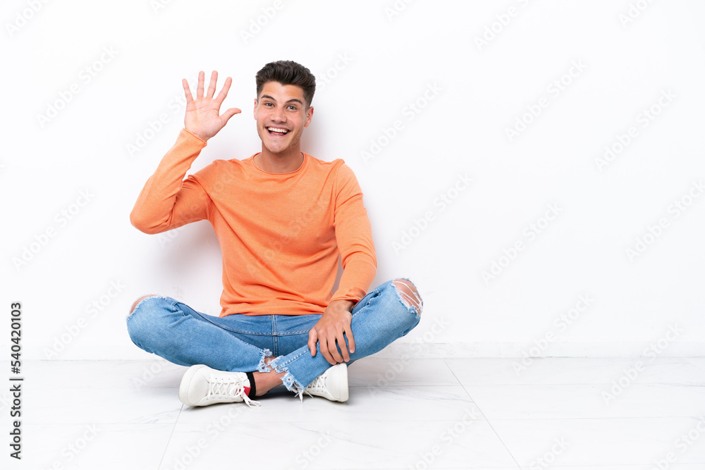 Young man sitting on the floor isolated on white background saluting with hand with happy expression Young man sitting on the floor isolated on white background saluting with hand with happy expression