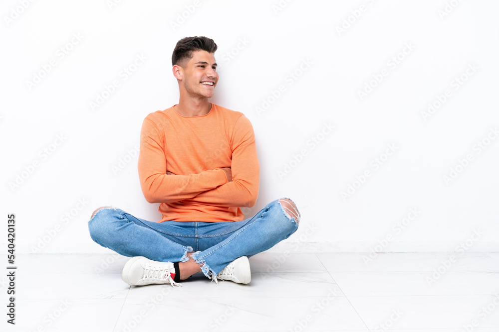 Young man sitting on the floor isolated on white background with arms crossed and happy Young man sitting on the floor isolated on white background with arms crossed and happy