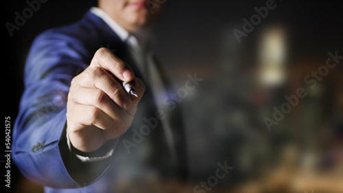 Businessman holding a pen to write on the screen to sign a contract or an agreement on blur background © Sakoodter Stocker