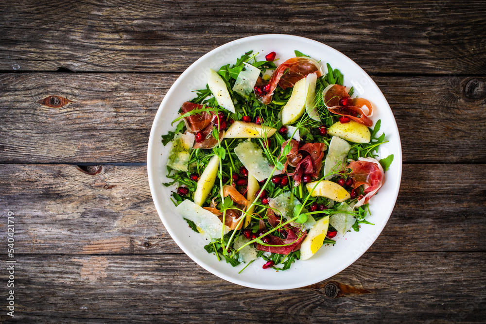 Fresh salad - prosciutto di Parma, pomegranate, pear, leafy vegetables and parmesan on wooden background
Fresh salad - prosciutto di Parma, pomegranate, pear, leafy vegetables and parmesan on wooden background