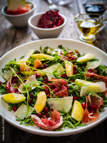 Fresh salad - prosciutto di Parma, pomegranate, pear, leafy vegetables and parmesan on wooden background
