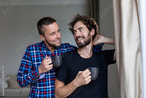 Young gay couple in love looking out the window. Two young androgynous men smiling together and having coffee. © Graphicroyalty